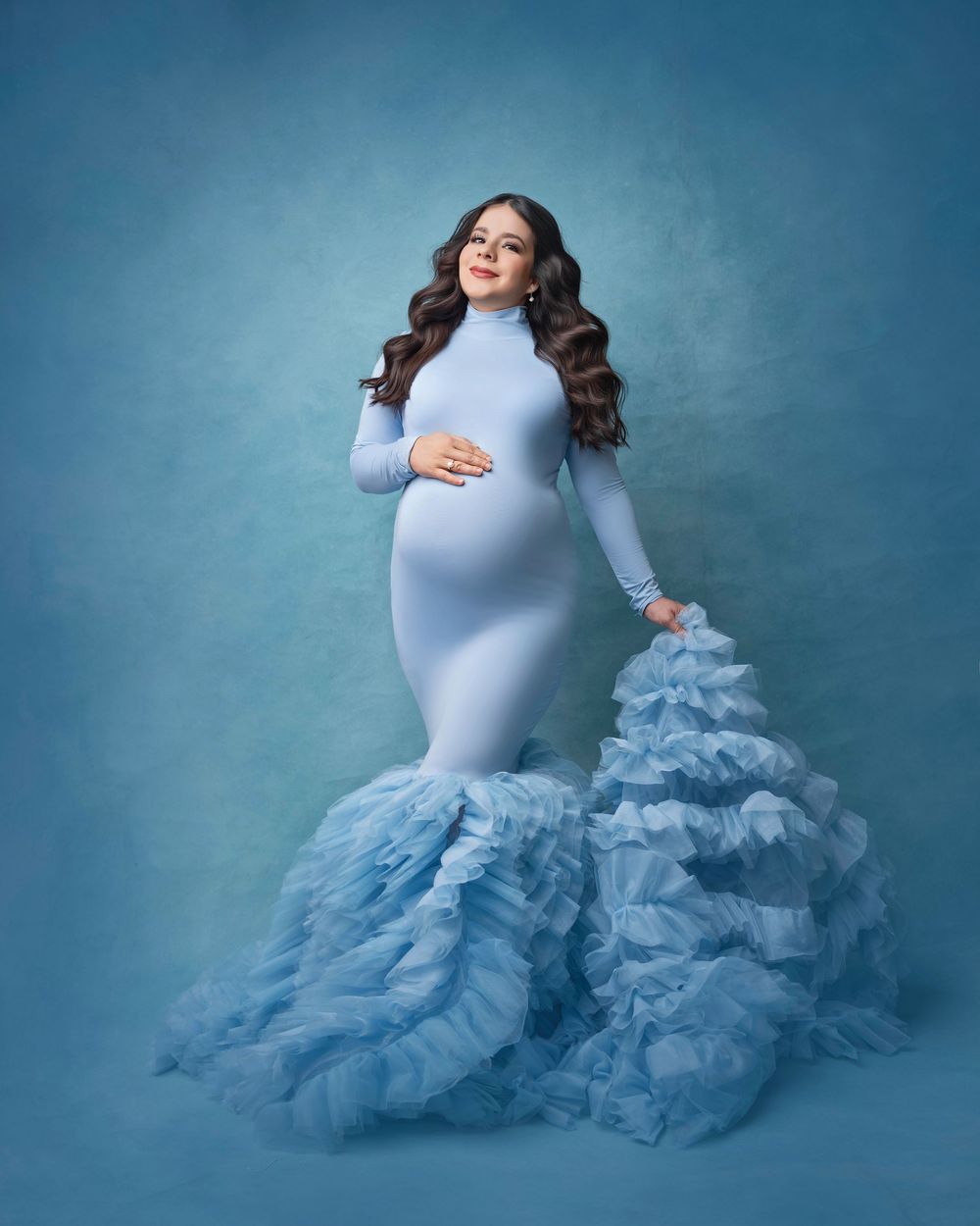 Maternity portrait in fitted blue gown with dramatic ruffled train.
