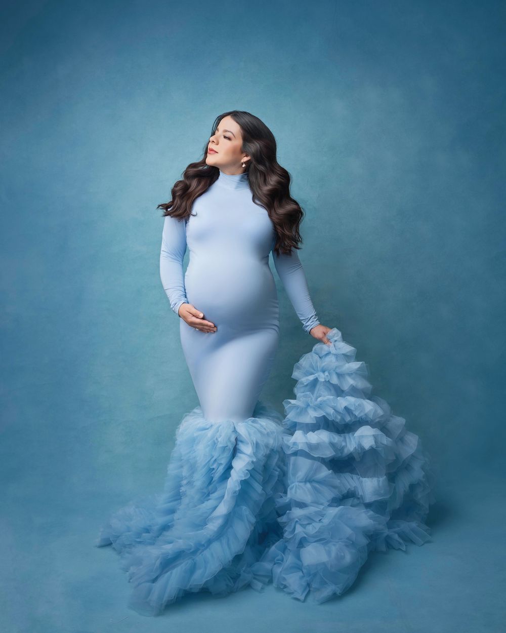 Dramatic maternity photo featuring light blue dress with cloud-like ruffled train.
