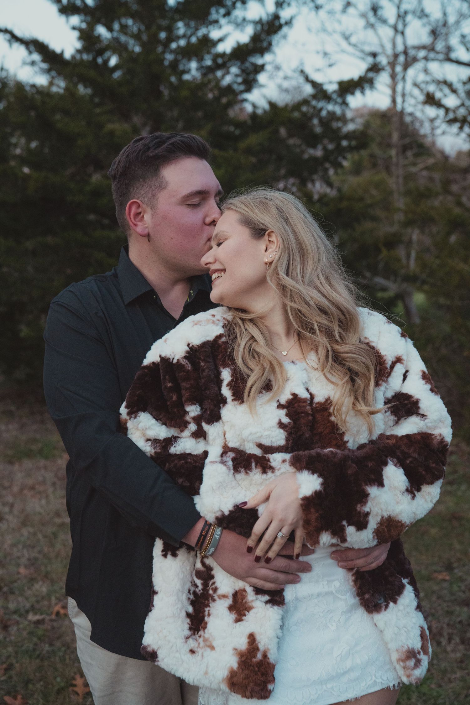 A couple in wedding attire embrace outdoors, with the bride wearing a unique white and burgundy dress.