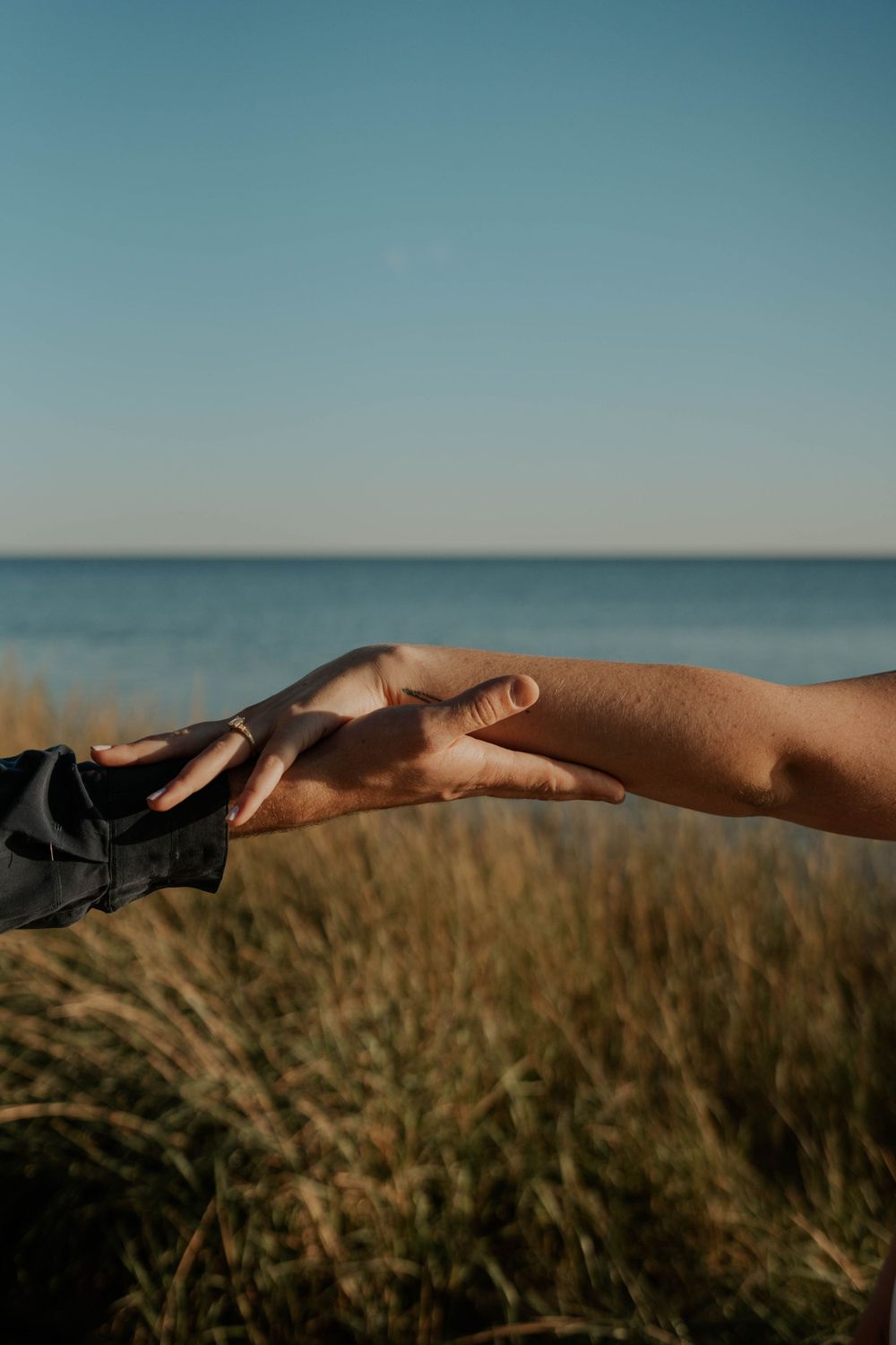 Close-up of two hands reaching toward each other against ocean backdrop.