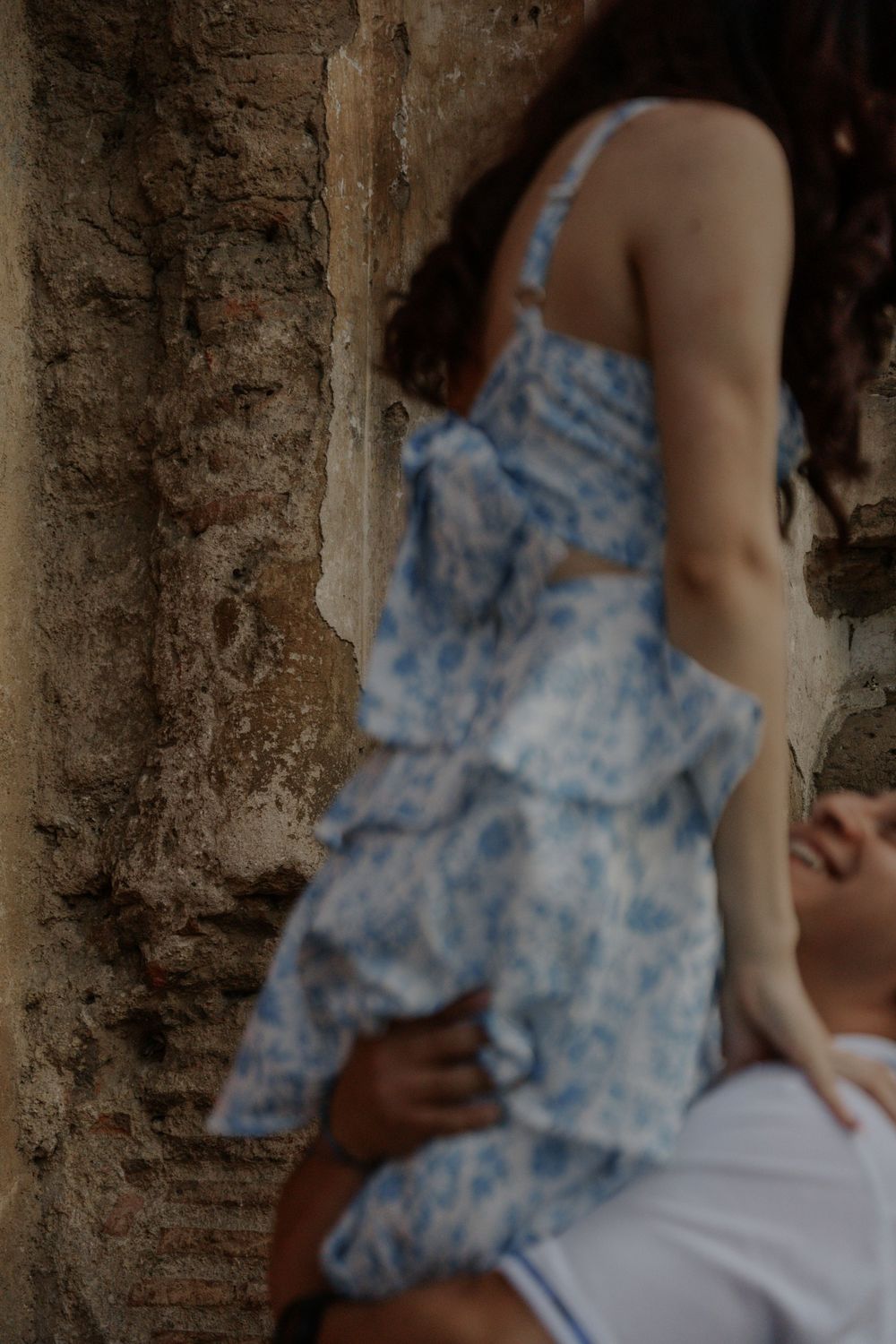 An artistic close-up shot captures details of a blue floral tiered dress against weathered stone.