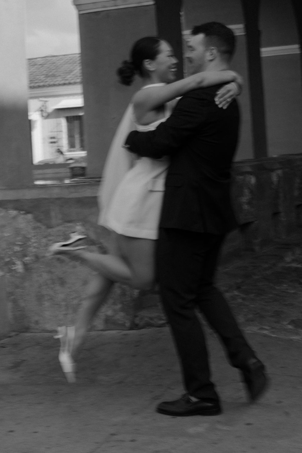 A playful black and white portrait of a couple dancing together.