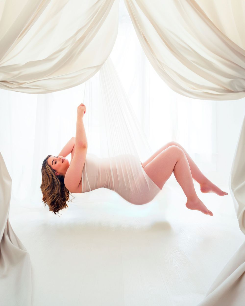 Figure draped in white fabric creates ethereal floating pose. Maternity Photos.