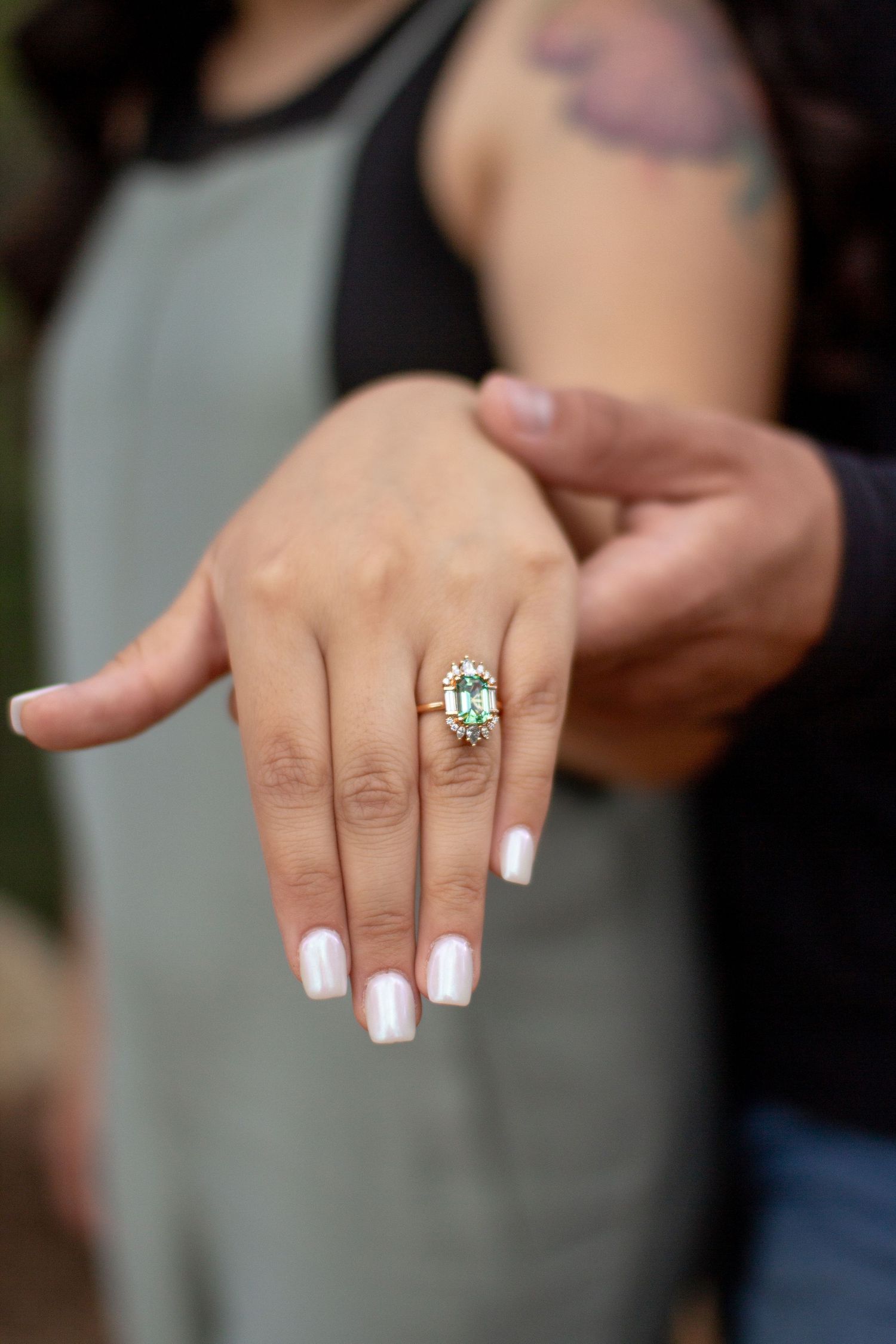 Hand displaying an elegant cushion-cut engagement ring with white nail polish and a black top visible in the background.