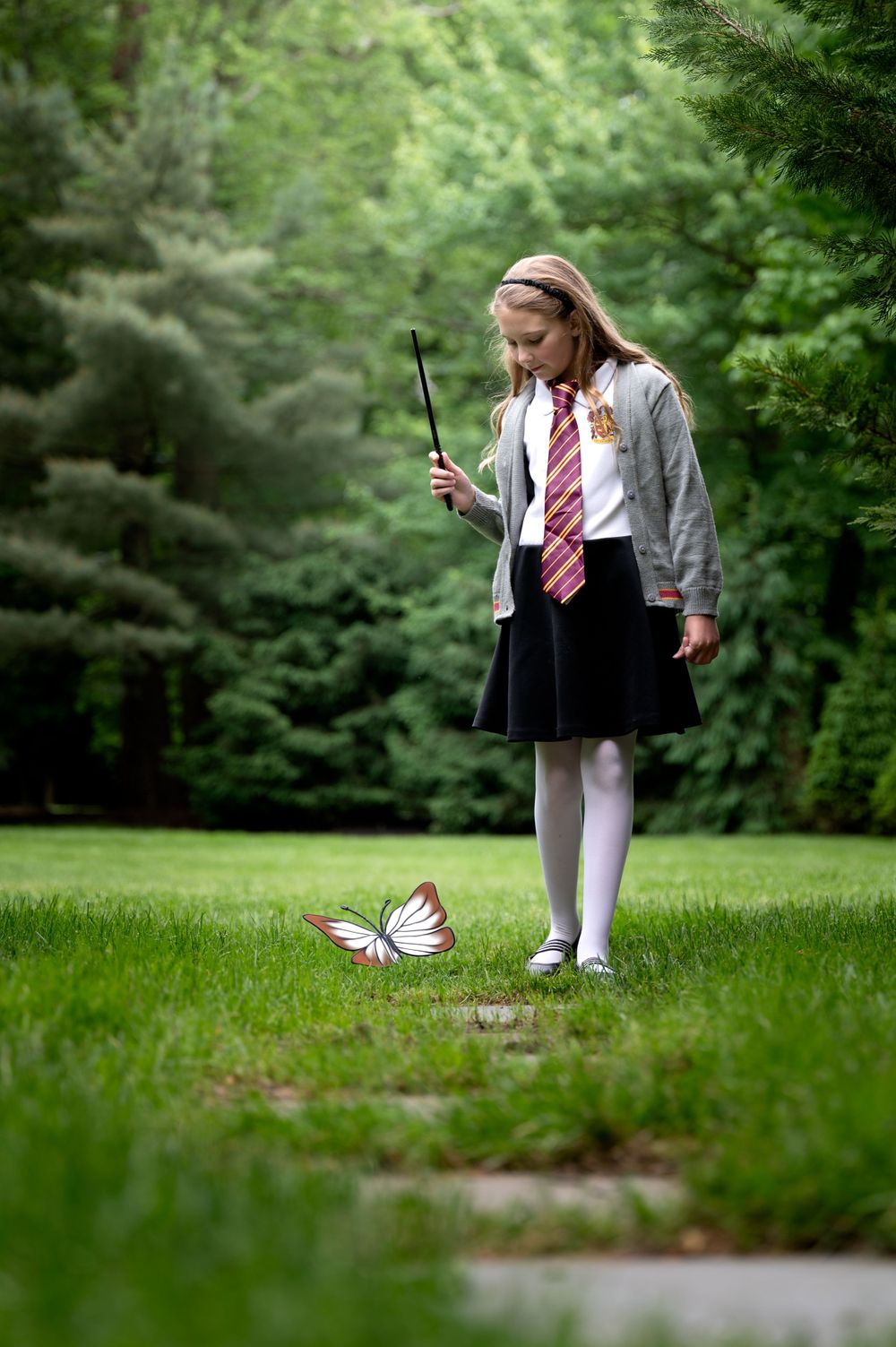 Student in school uniform with wand looking at butterfly in magical forest scene.