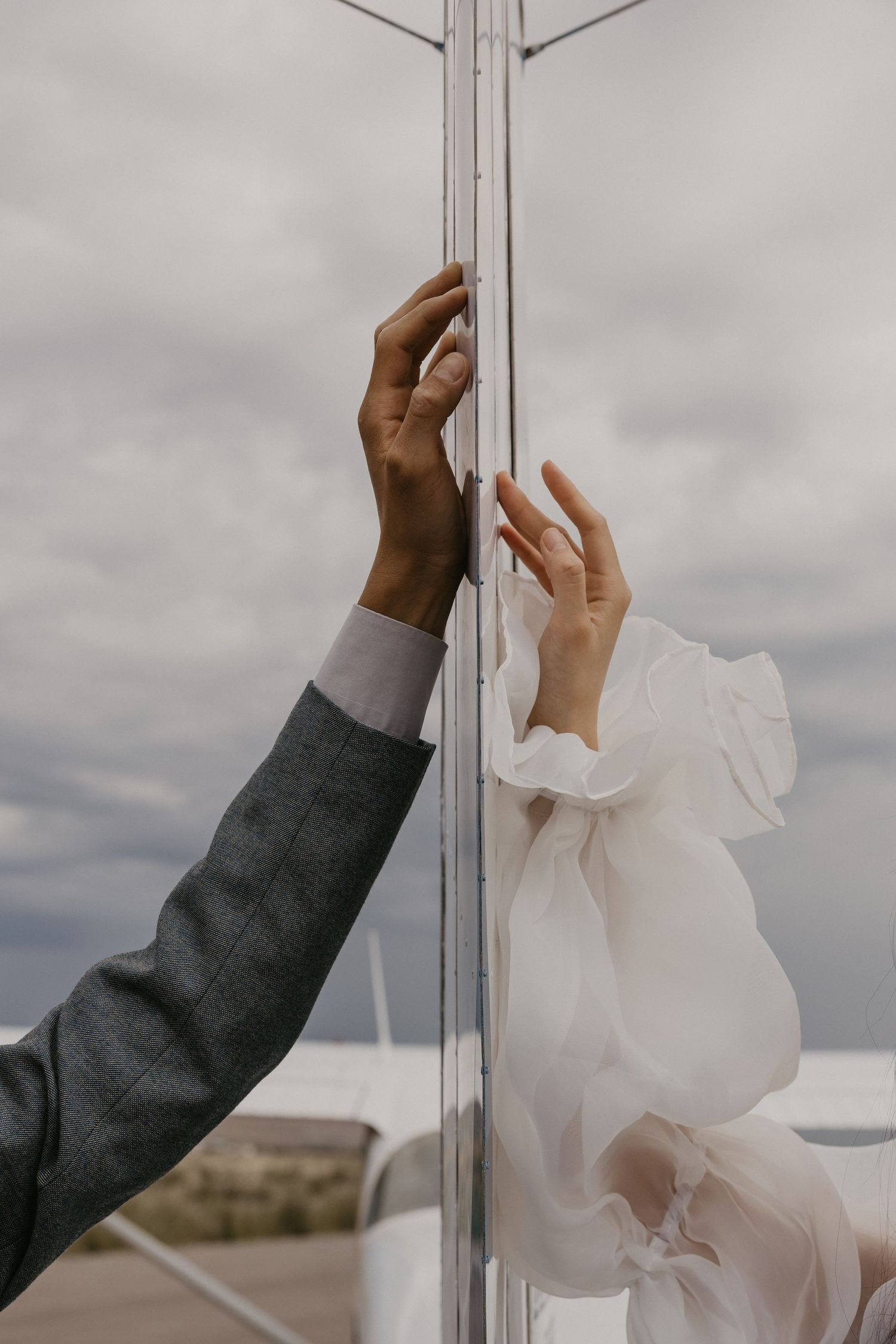 Artistic shot of hands reaching across glass divider in dramatic lighting.