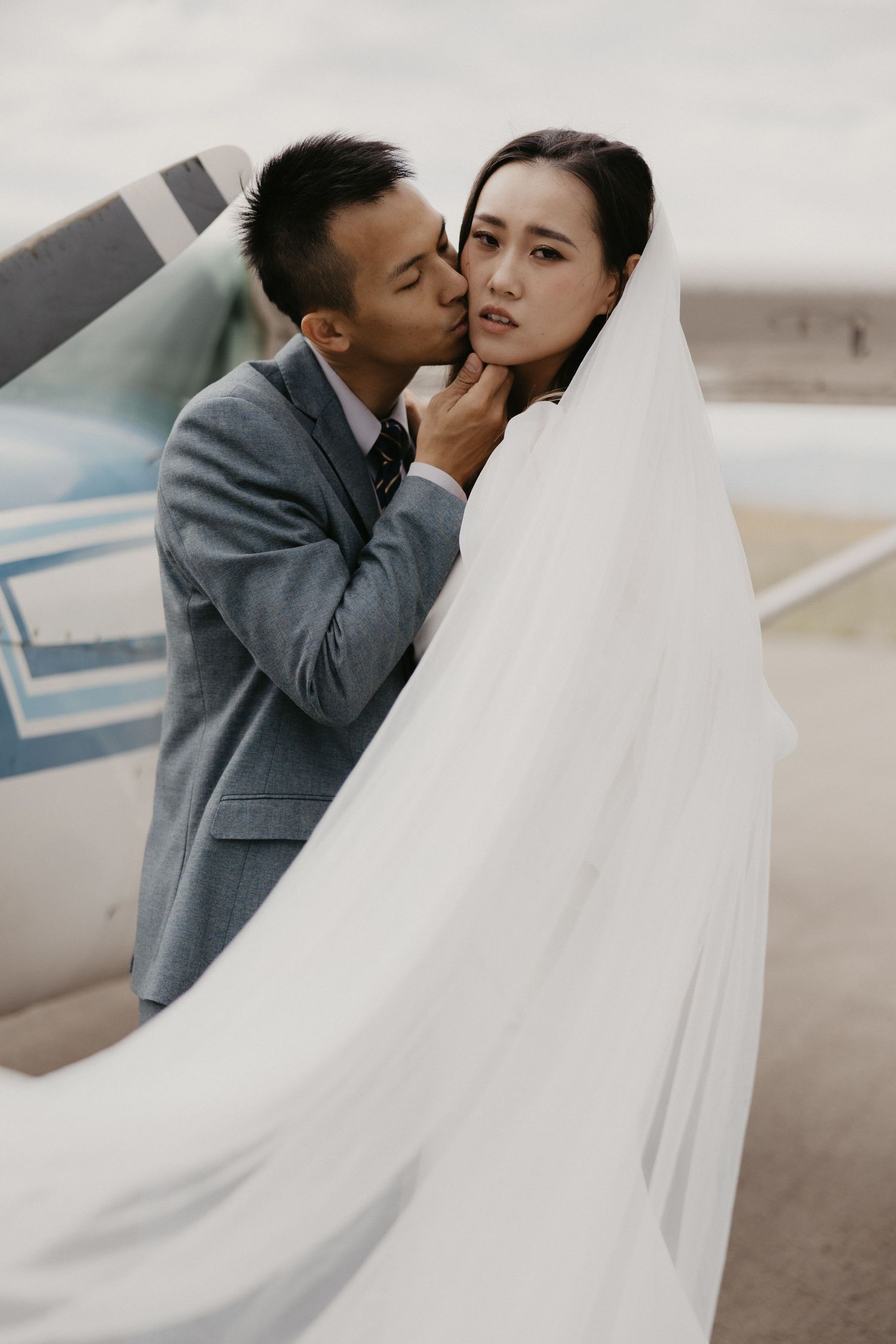 Wedding couple embraces near small aircraft with flowing white veil. Aviation Elopement, Utah, Stintson Airport, San Antonio