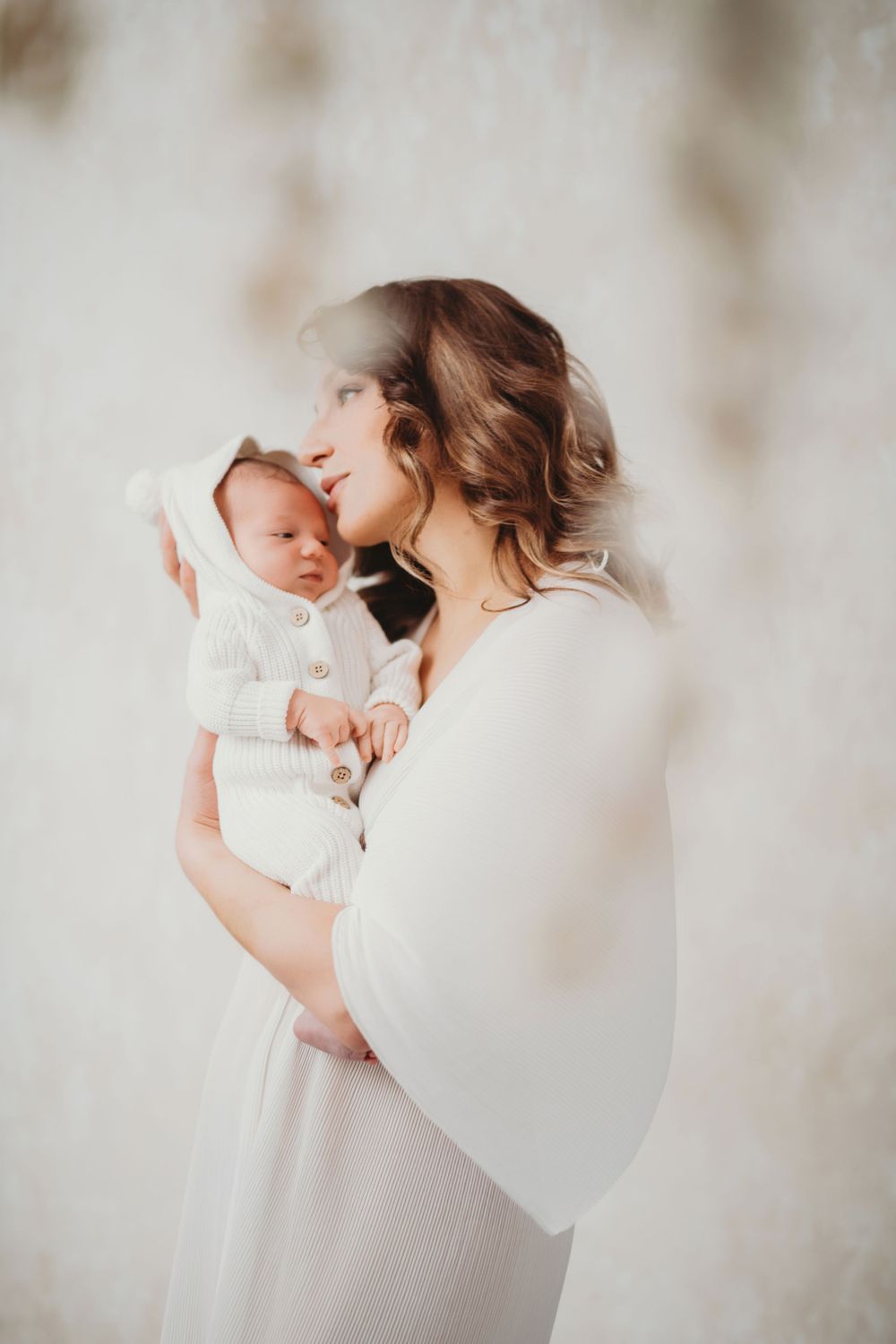 A tender moment captured in soft light as a mother in white holds her sleeping newborn baby against her chest in Bellevue studio.