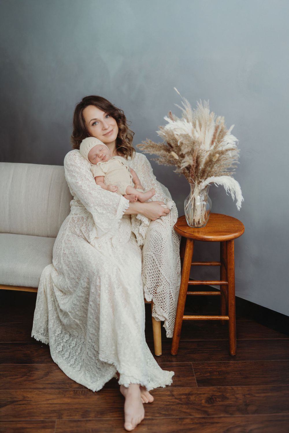 A tender moment captured in a white dress with pampas grass decor on wooden stool against grey wall interior in Bellevue studio .