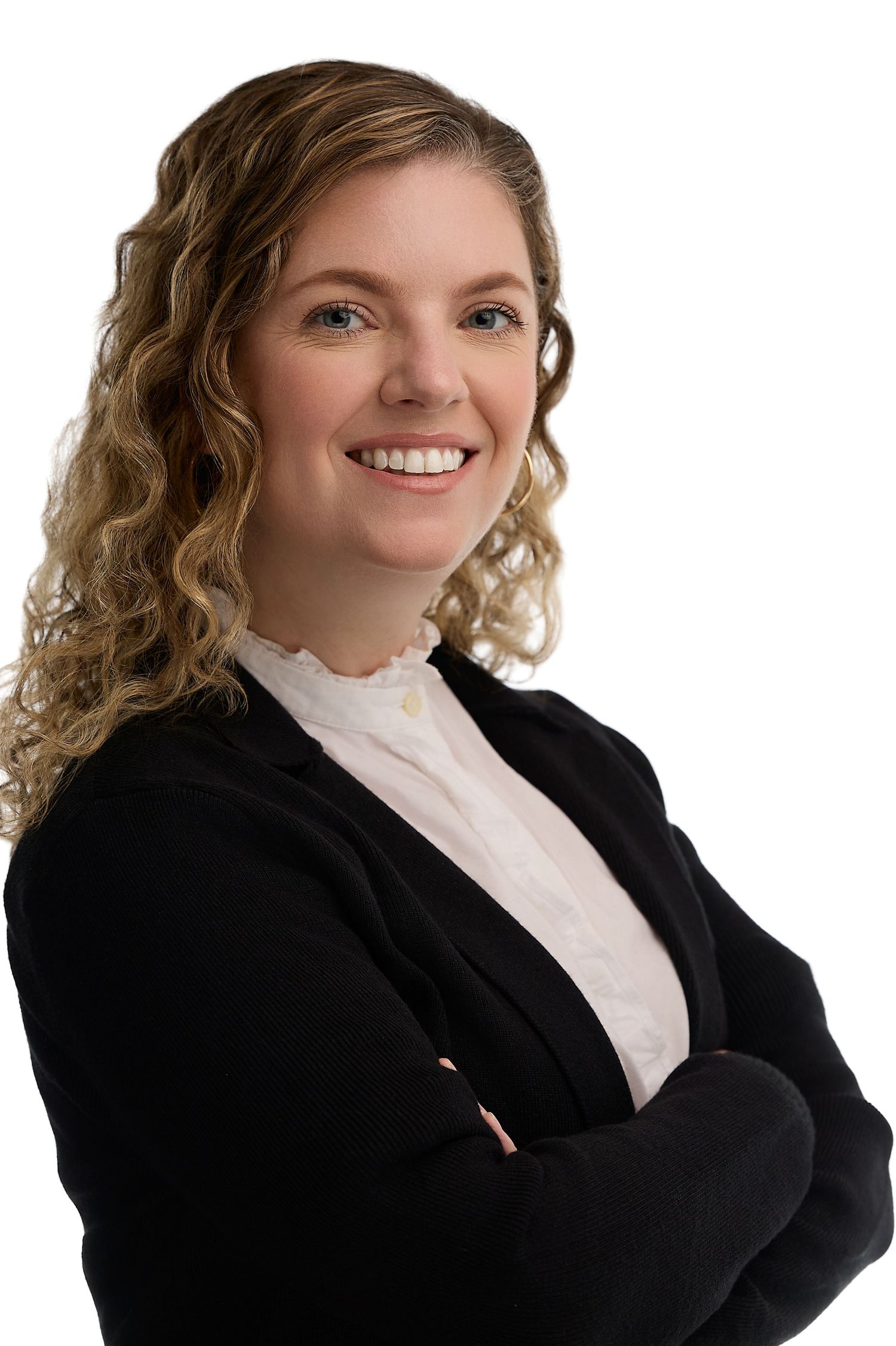 Professional woman with curly blonde hair smiling confidently with arms crossed, wearing a black blazer and white blouse.