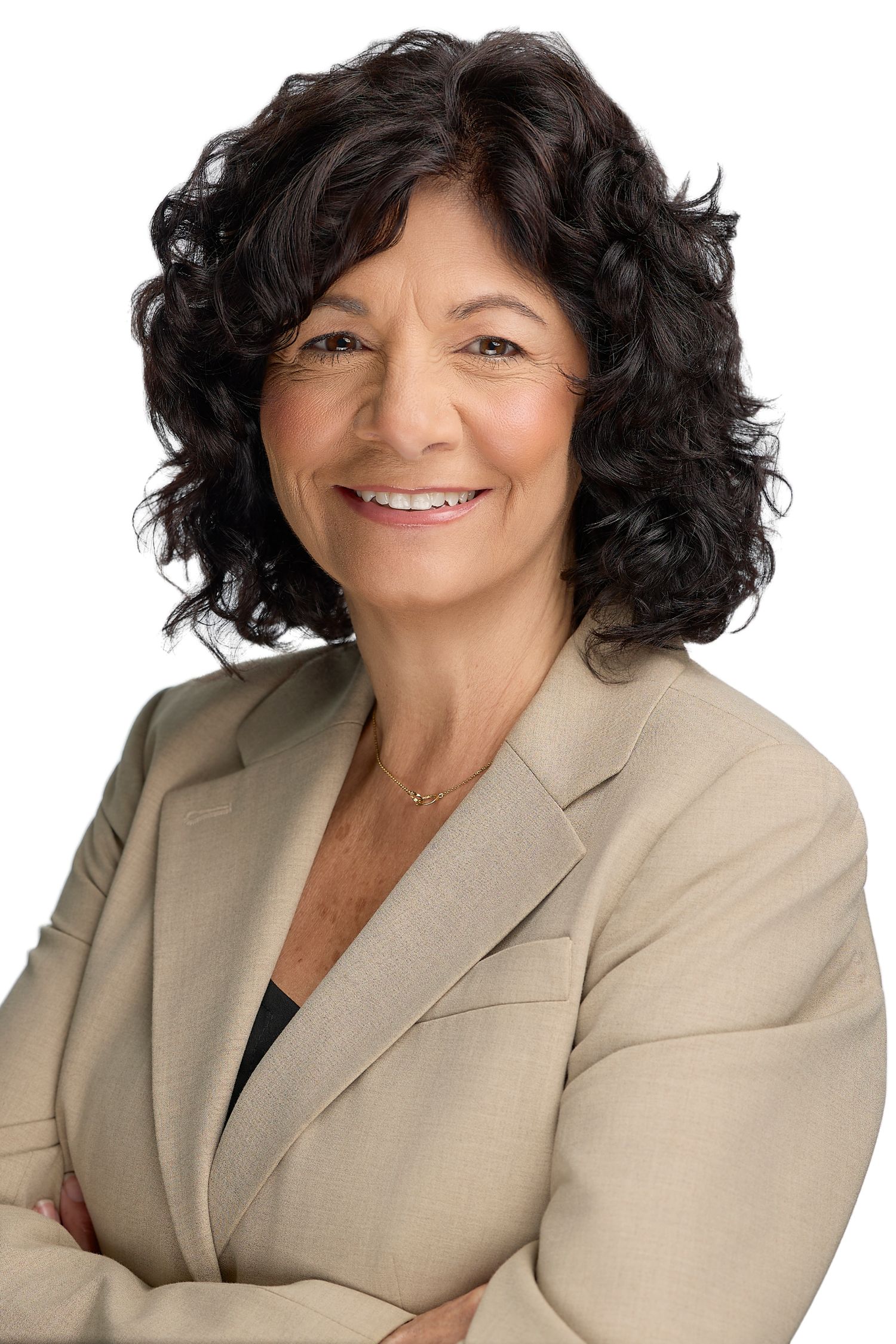 Professional headshot of a smiling middle-aged woman with curly dark hair wearing a beige blazer, arms crossed.
