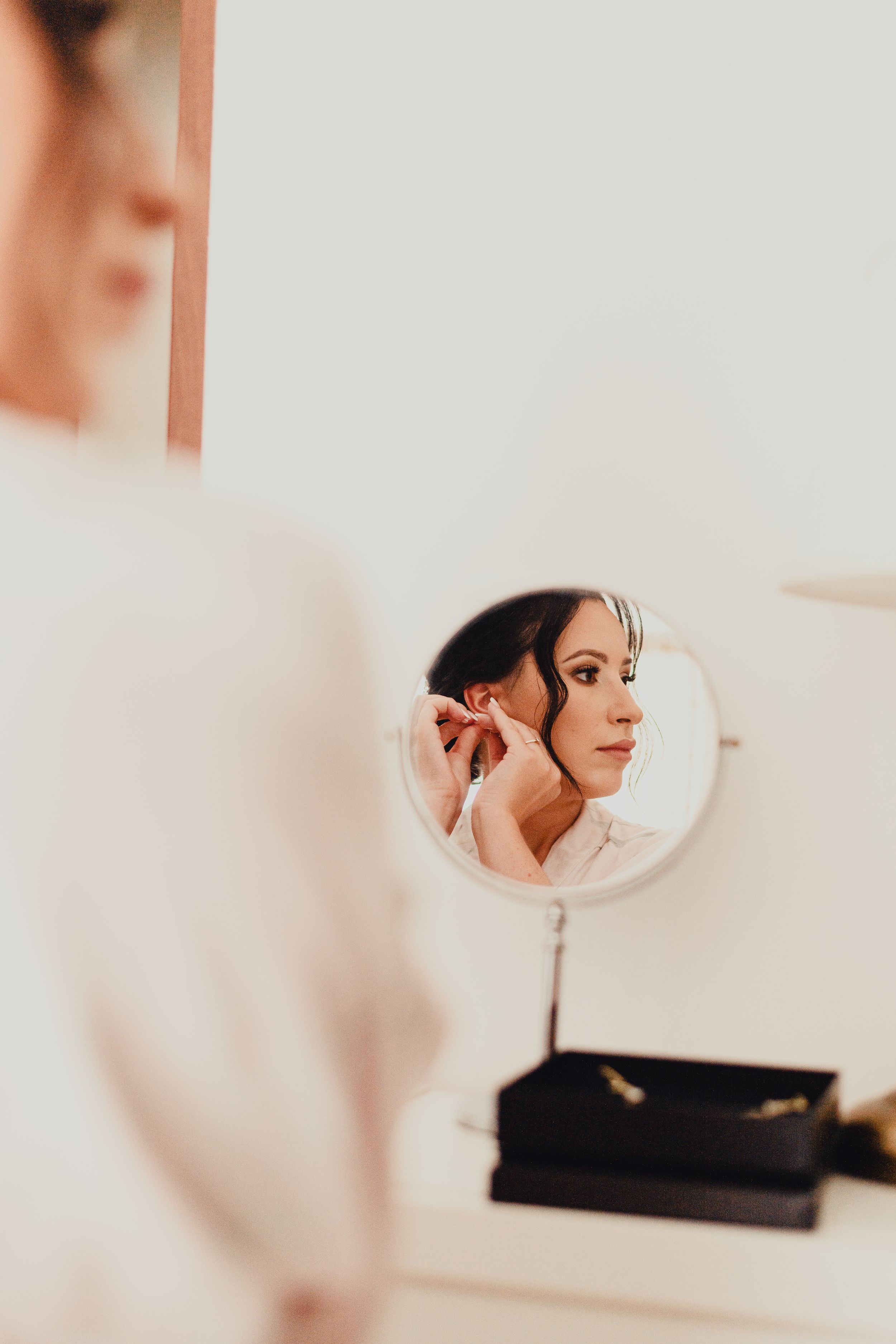 Bridal preparation scene reflected in vanity mirror with soft natural lighting.
