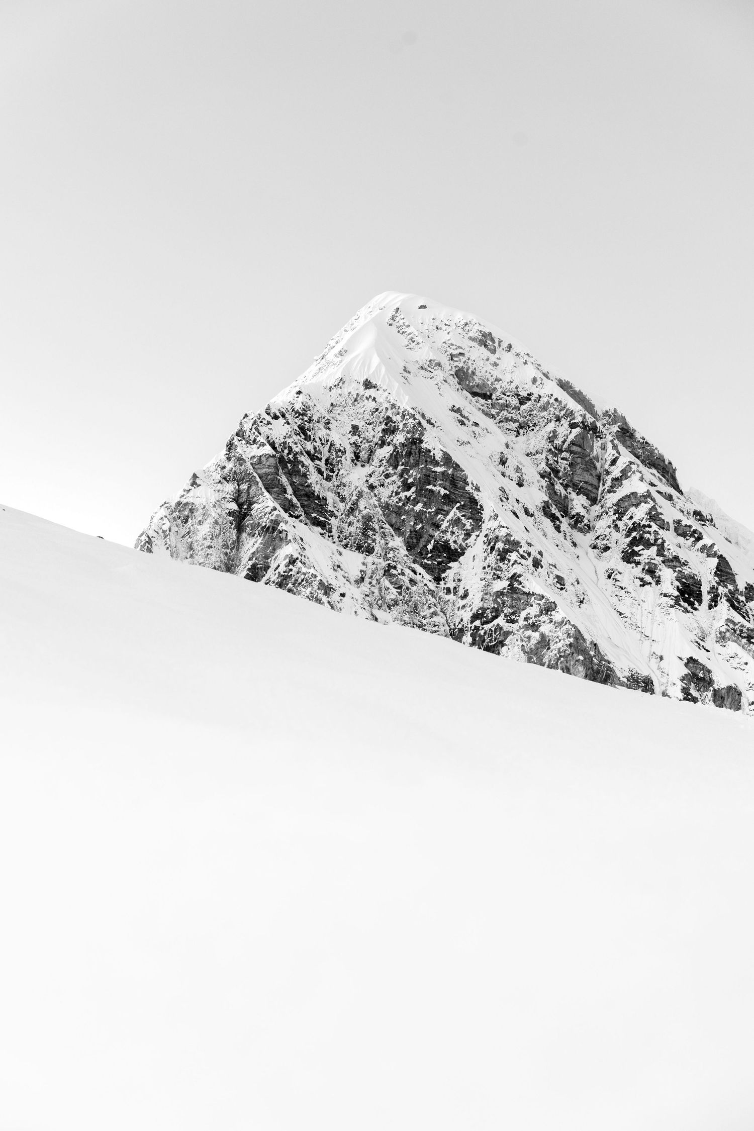 Minimalist black and white landscape of snow-covered mountain peaks against a light sky.