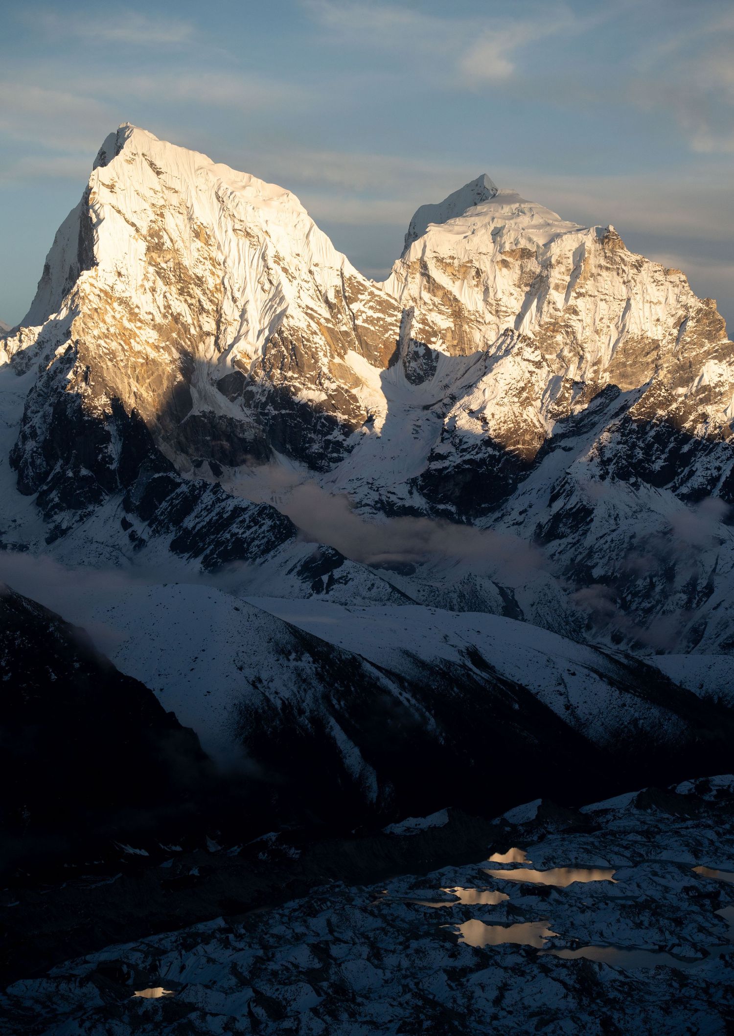 Majestic snow-covered mountain range glows in golden sunlight during sunset or sunrise.