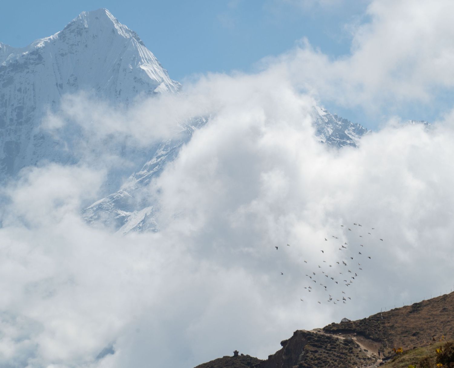 Snow-capped mountain peaks rise dramatically against a cloudy blue sky in a panoramic landscape view.