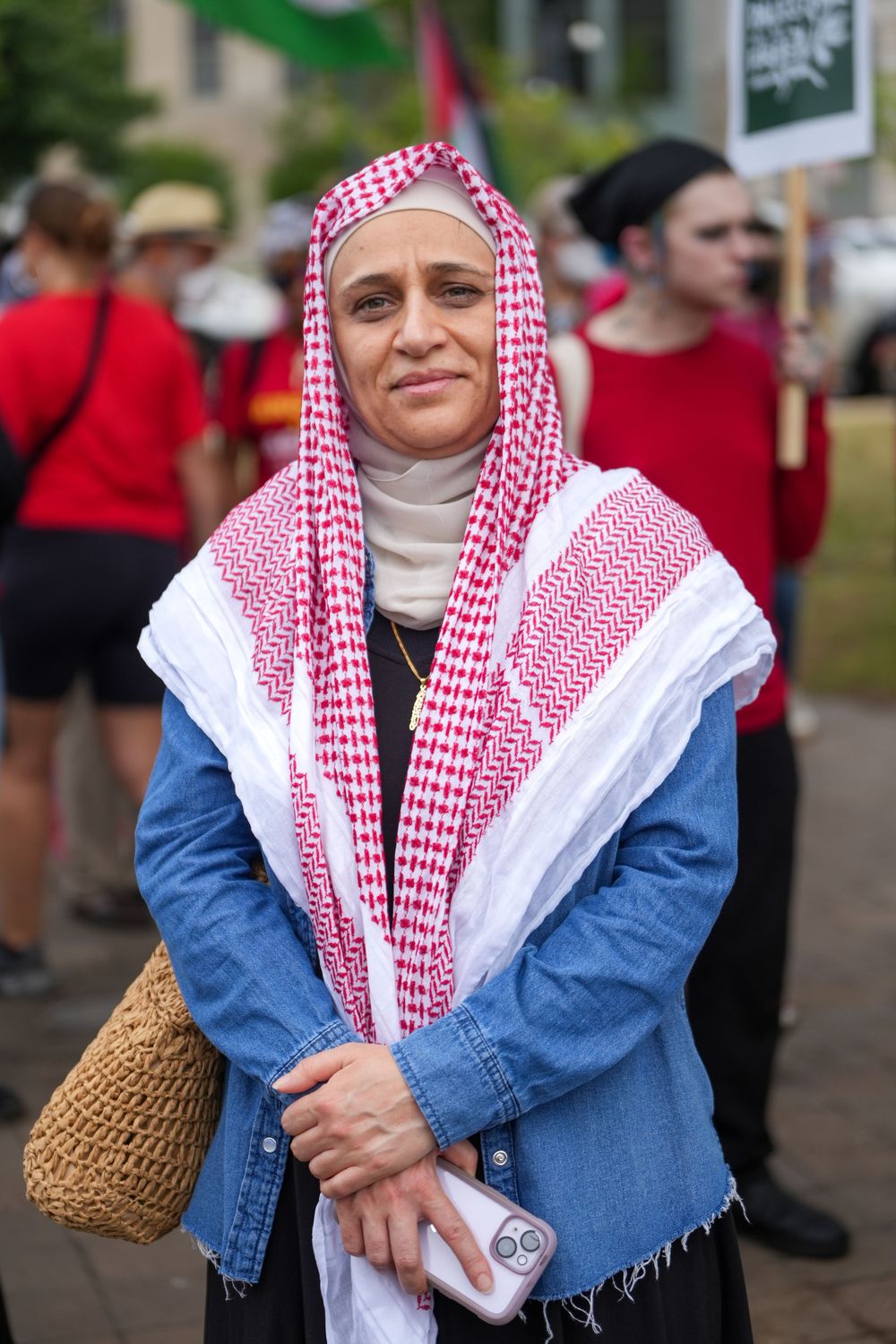 Someone wearing a traditional red and white keffiyeh headscarf with denim jacket at a public gathering.