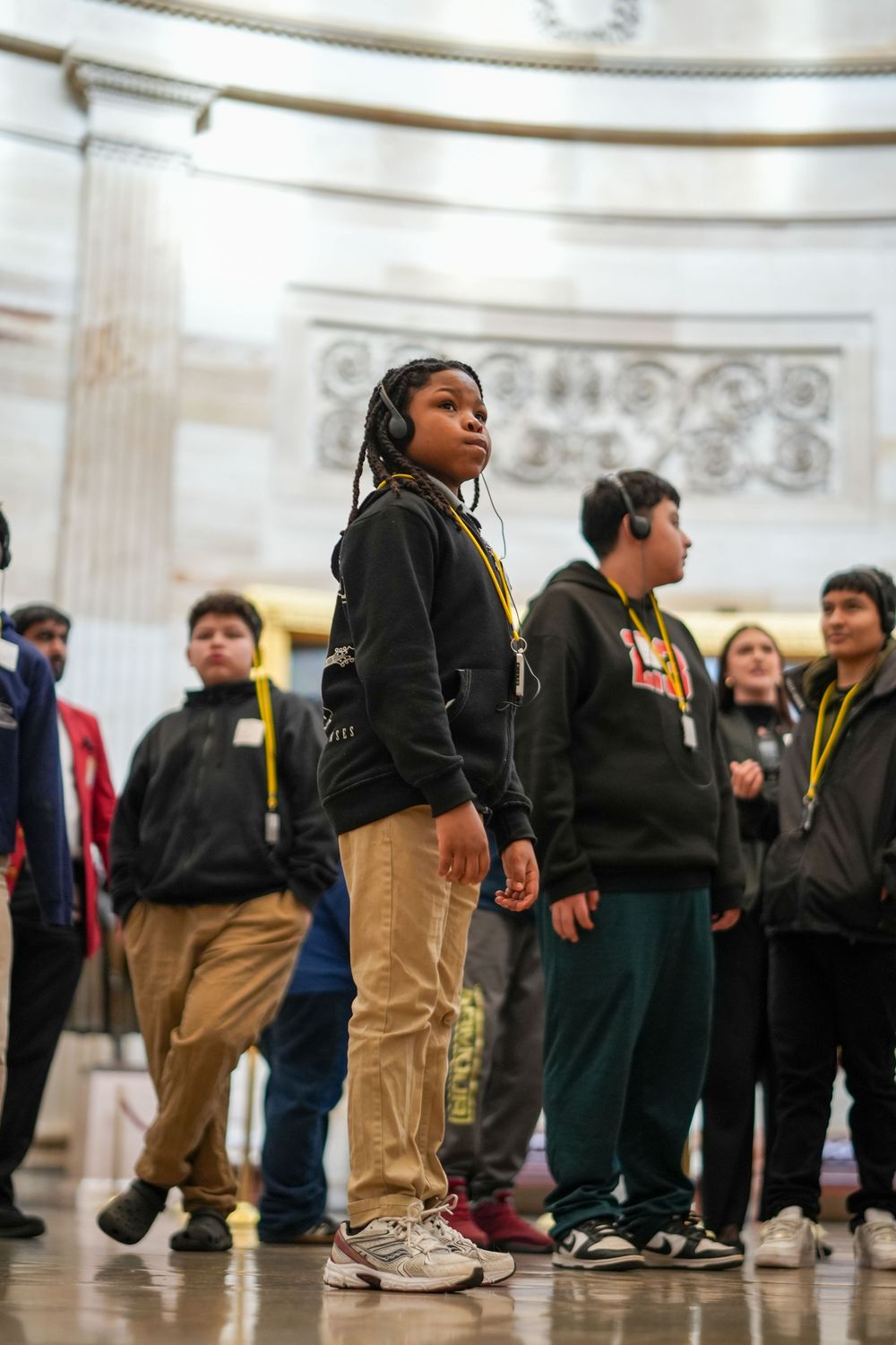 Students on a school field trip listen to audio guides in a grand rotunda building with classical architecture.