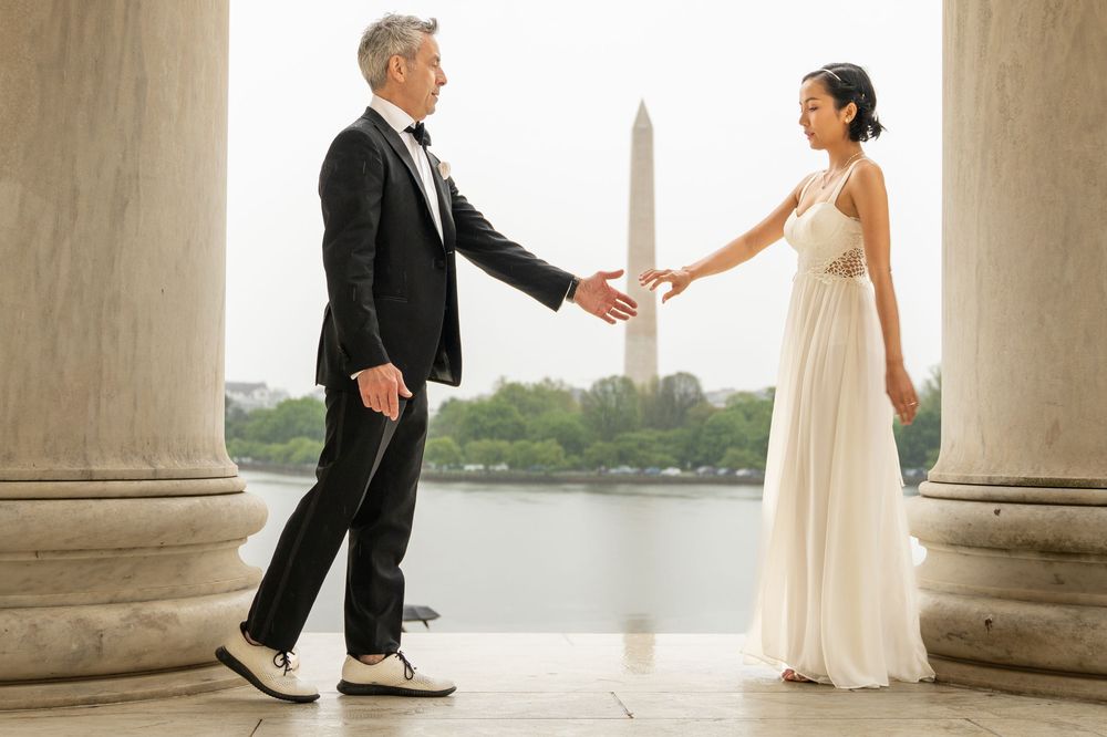 Bride and groom holding hands at Jefferson Memorial with Washington Monument in background.