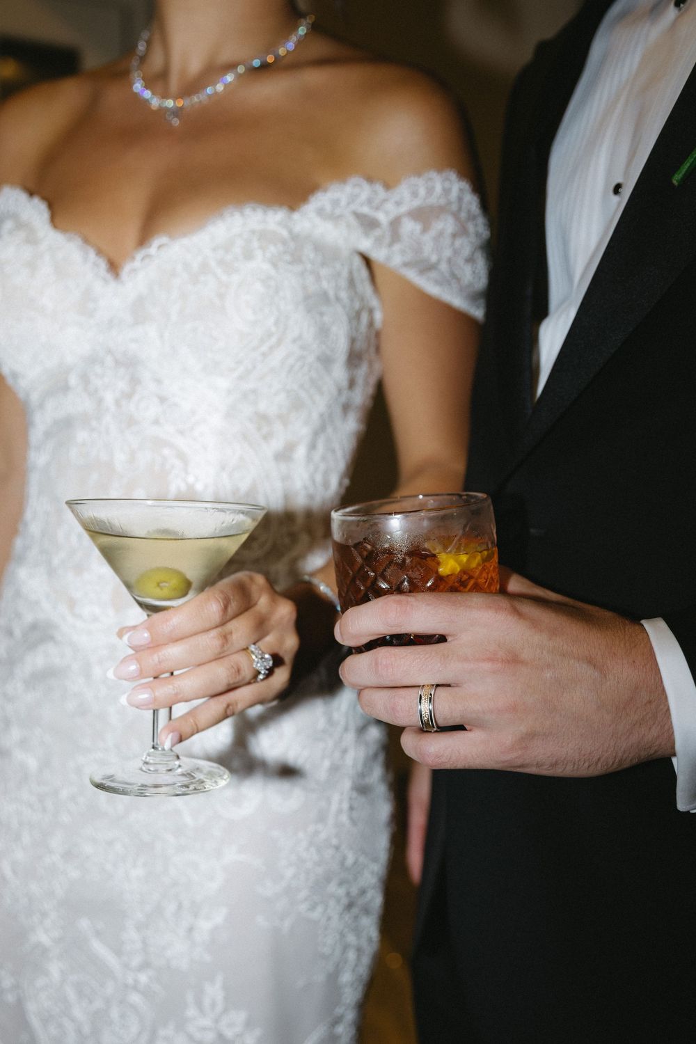 Close-up of wedding attire with crystal necklace and cocktail glasses being held.