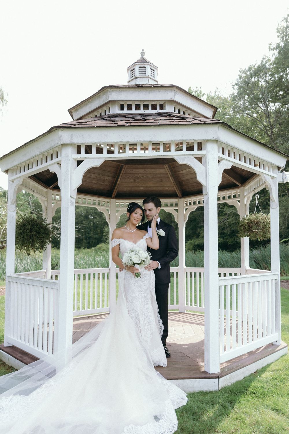 Wedding couple shares intimate moments in white gazebo surrounded by greenery.
