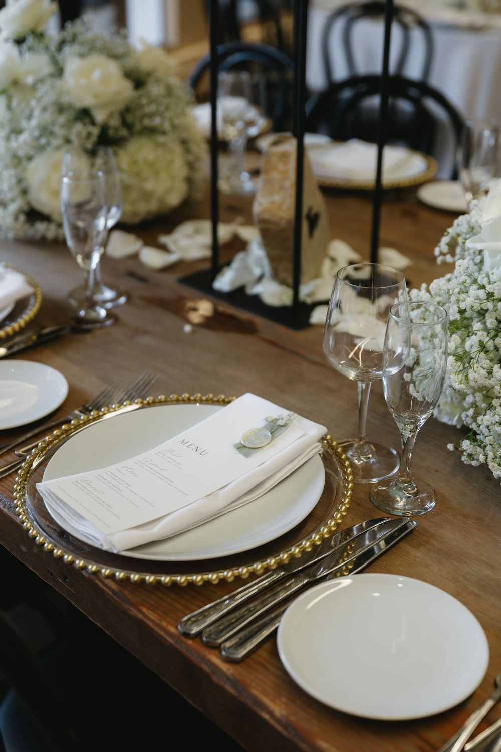 Elegant table setting with gold charger plates, white dinnerware, and delicate floral arrangements on a wooden surface.