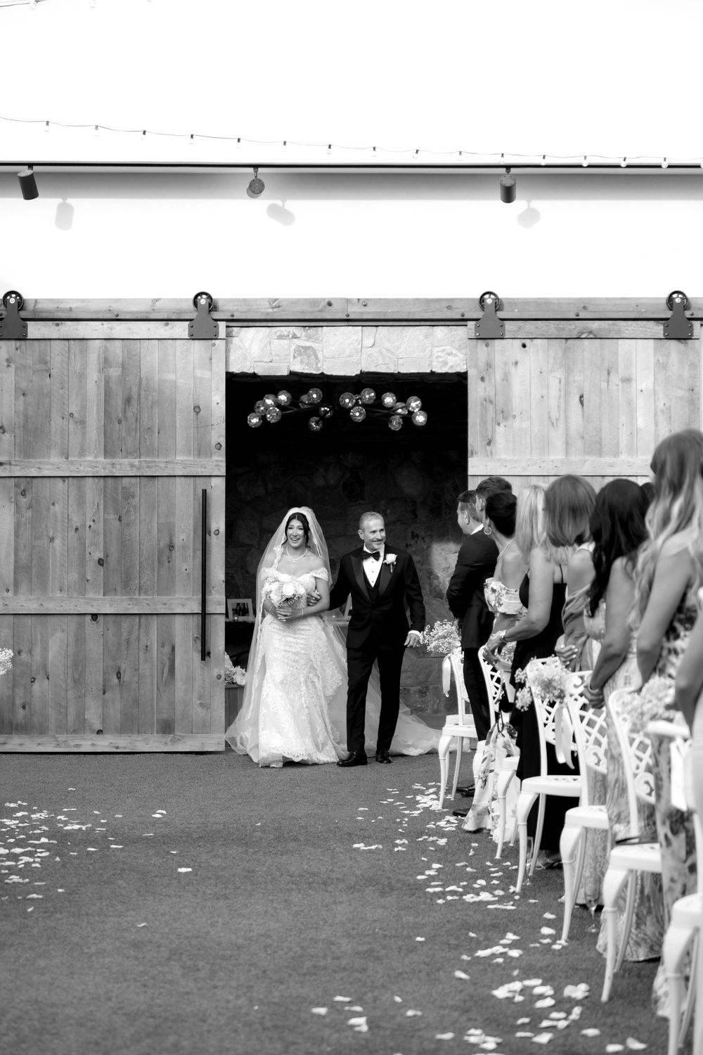 Wedding ceremony procession in black and white with flower petals scattered along the aisle.