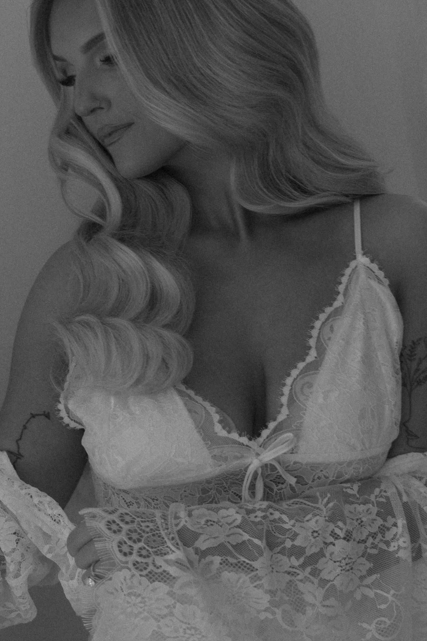 Bride in a strapless satin wedding gown with a high slit stands by a large window.