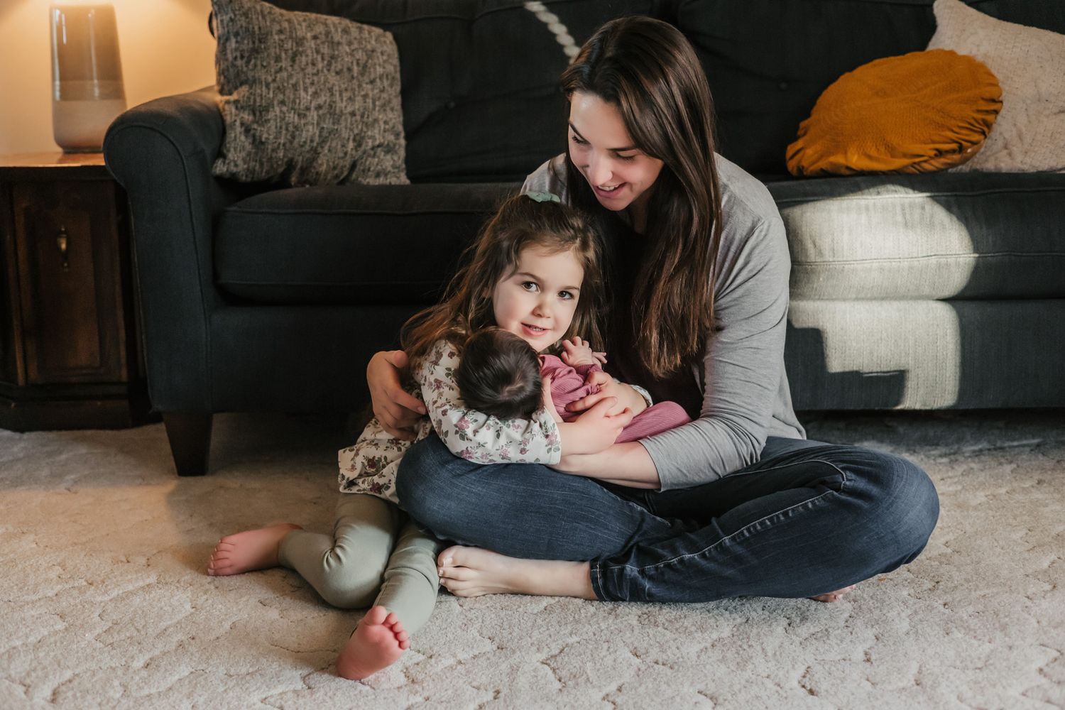 Parent and child share tender moment sitting on floor together with couch and pillows in background.