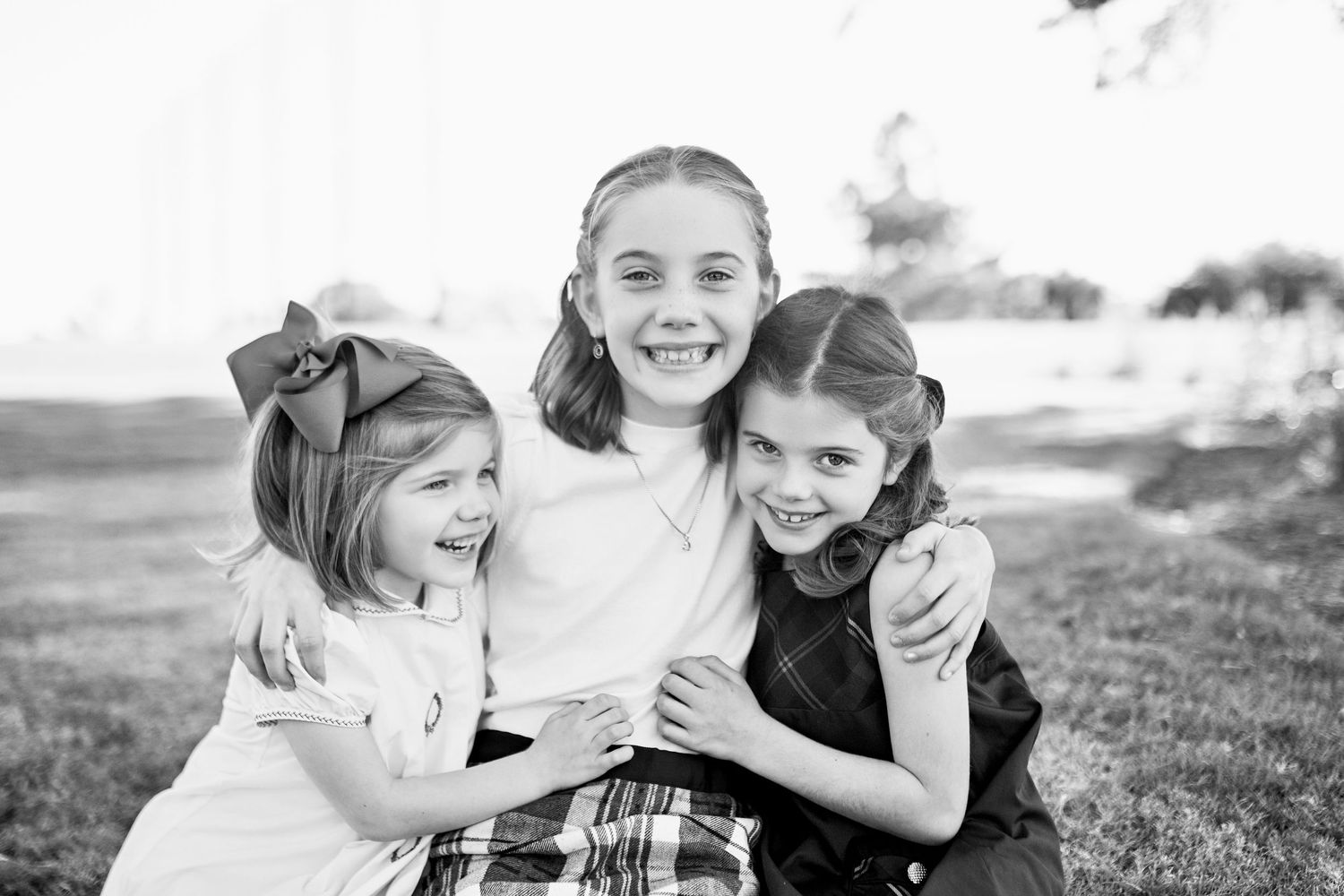 Three children share a joyful moment together outdoors in a heartwarming black and white portrait.