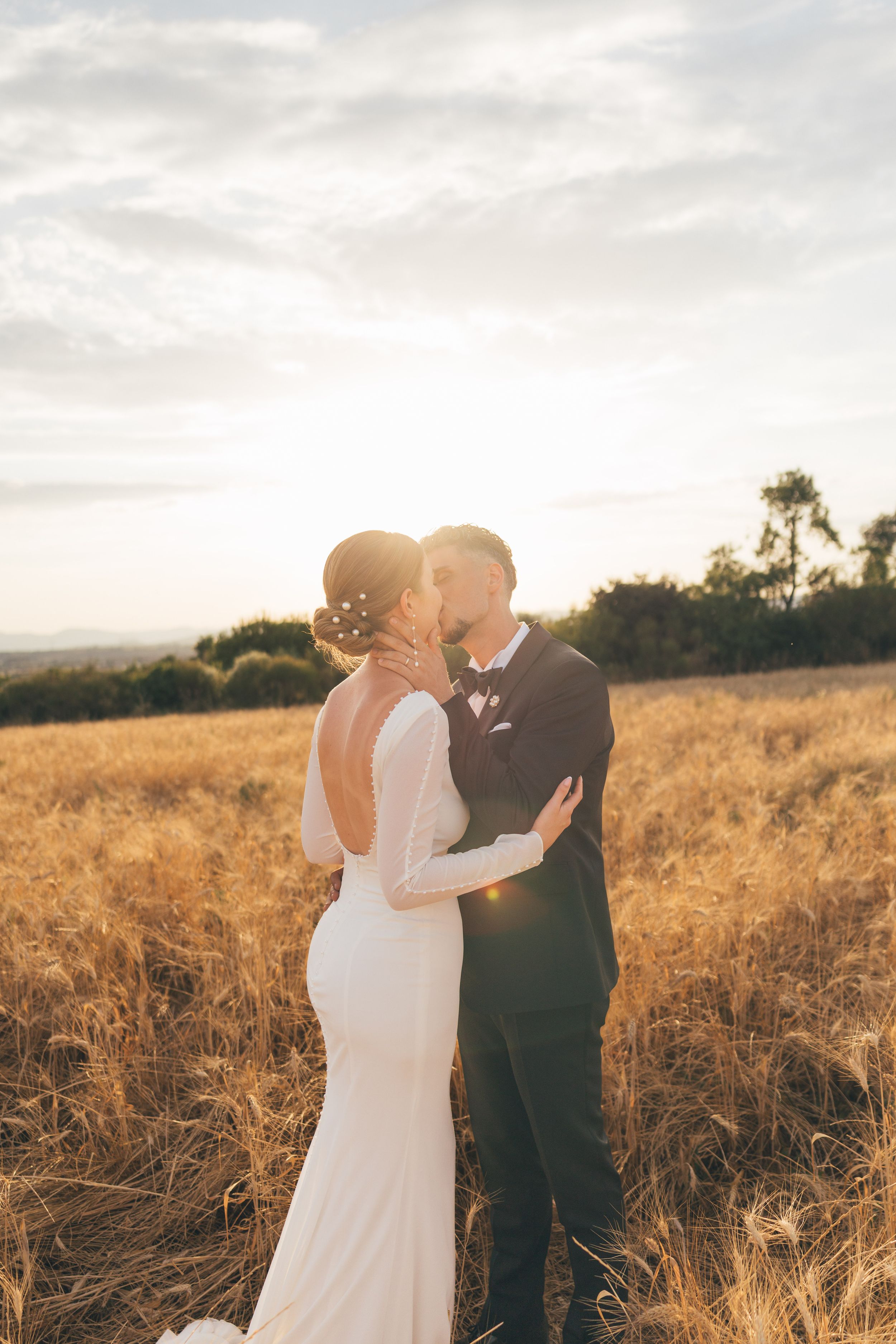 A couple shares a romantic moment in a golden field at sunset as warm light illuminates the tall grass around them.