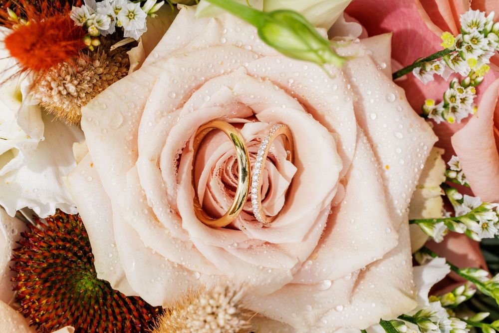 Deux alliances en or nichées dans une rose tendre entourée de fleurs mélangées dans un bouquet de mariée.