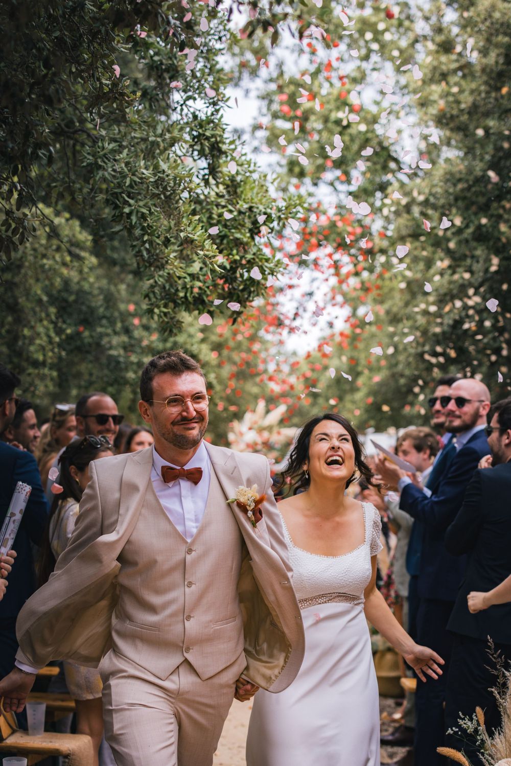 Un couple de jeunes mariés rient lors d'une cérémonie de mariage, entouré d’invités. Meilleur photographe mariage Hérault