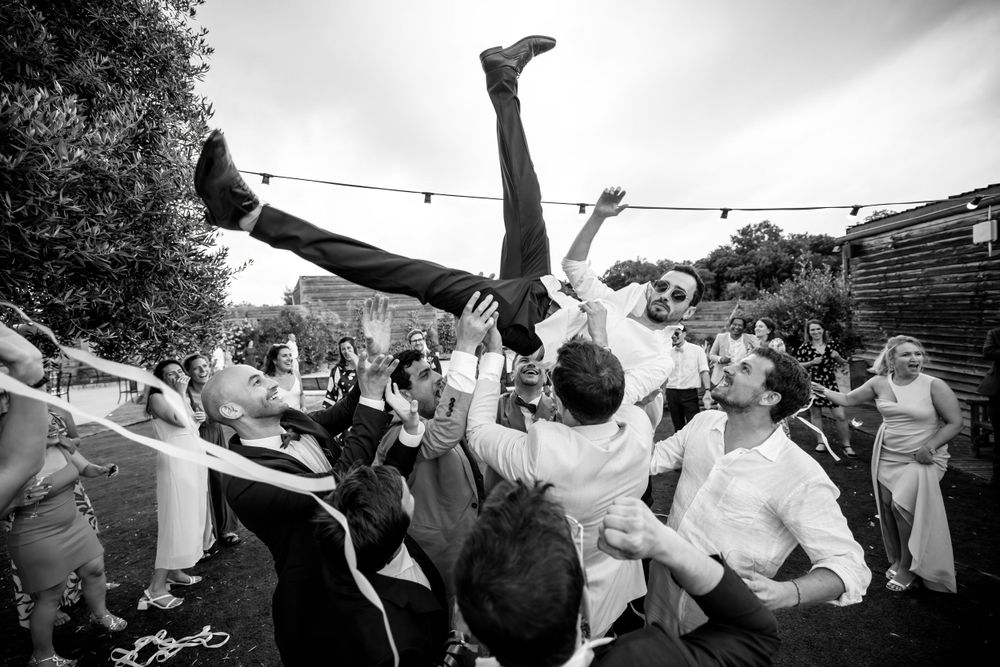 Une foule jette quelqu’un lors d’un mariage énergique en plein air en photographie noir et blanc. Photographe mariage Marseille
