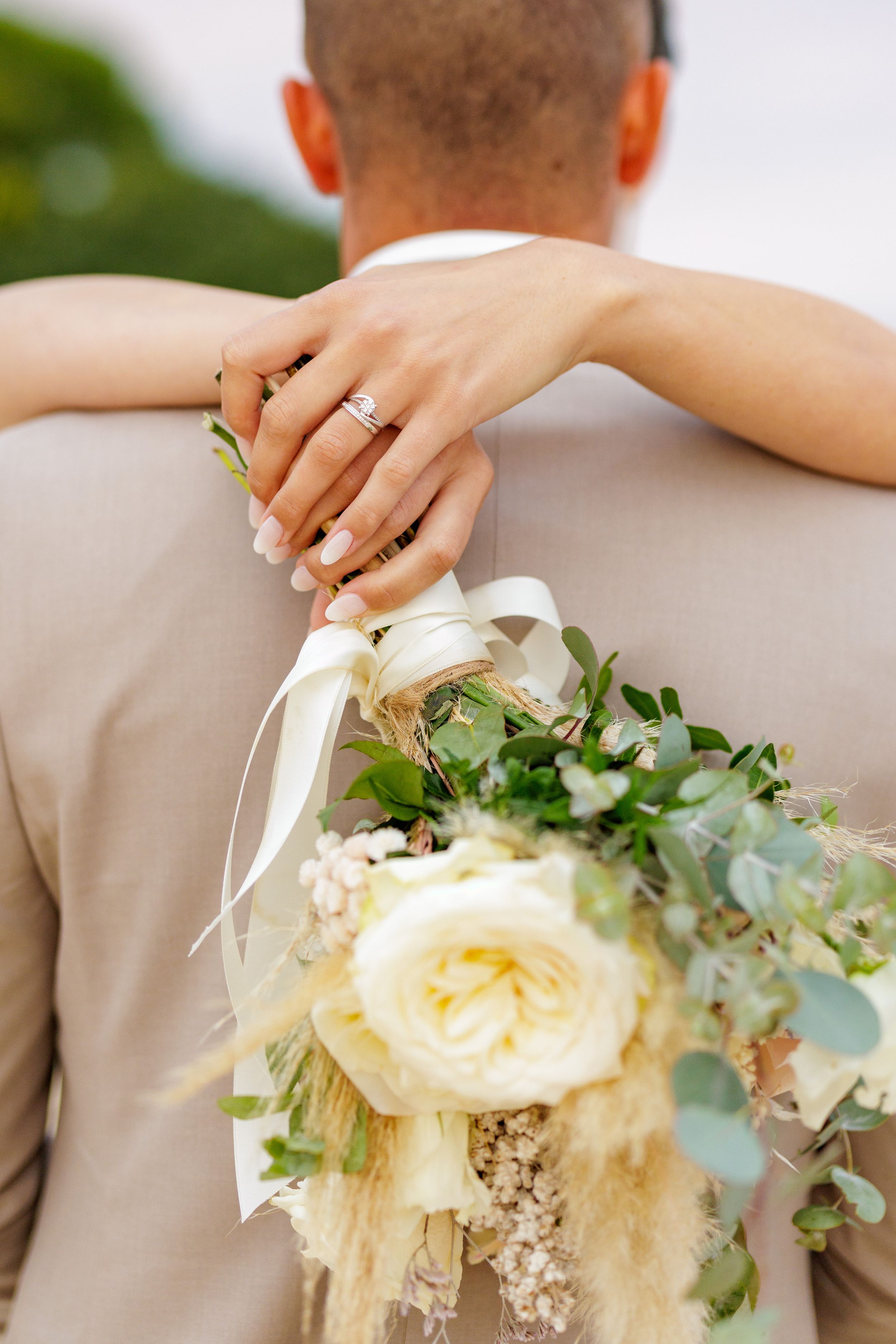 Close-up view of a wedding bouquet with cream roses and greenery resting against a beige suit jacket.