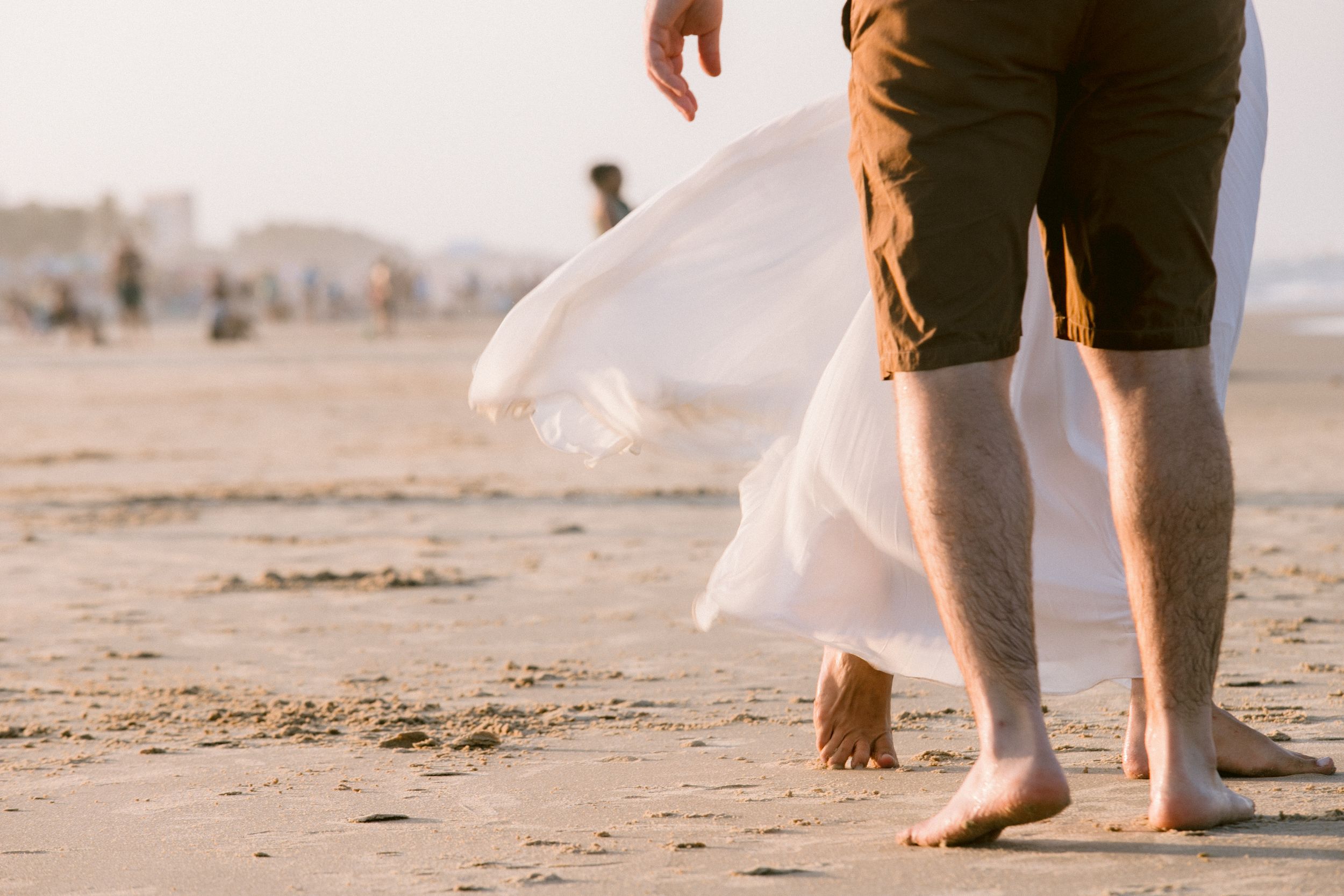 Bare feet walking on beach sand with flowing white dress fabric.
