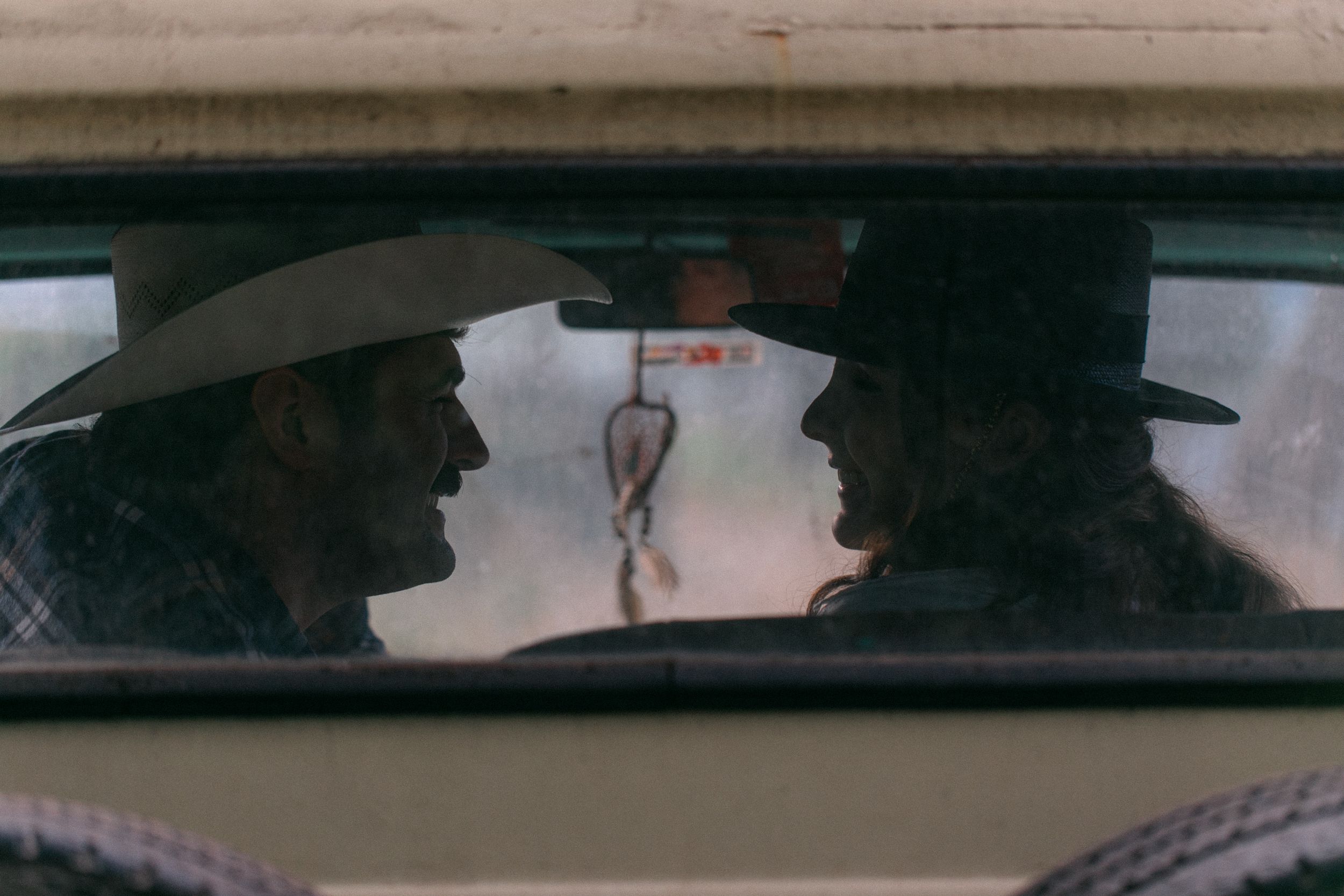 Silhouettes visible through a vintage car windshield at dusk.
