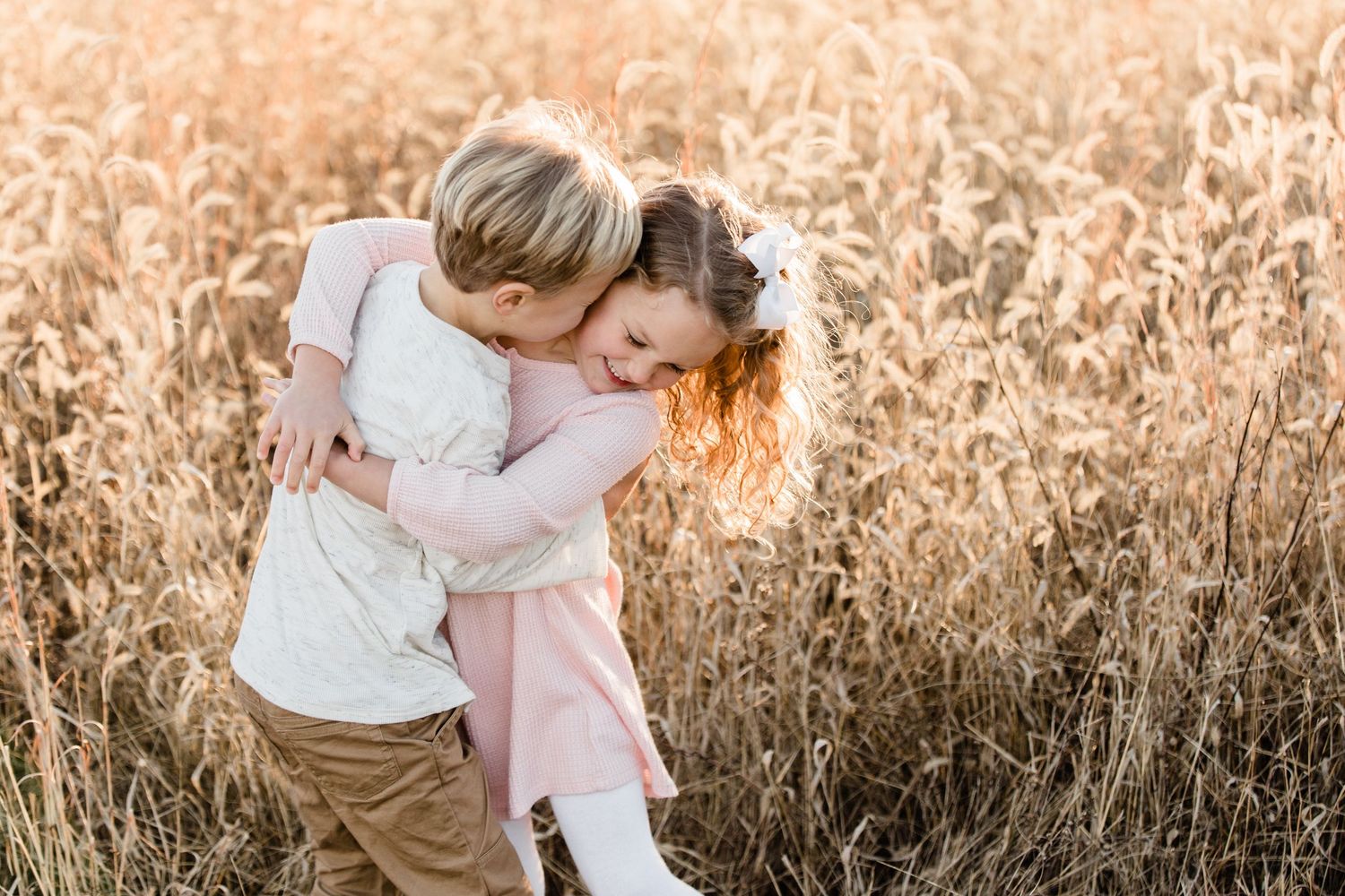 Family shares tender embrace in golden field at sunset as sunlight filters through tall autumn grass.