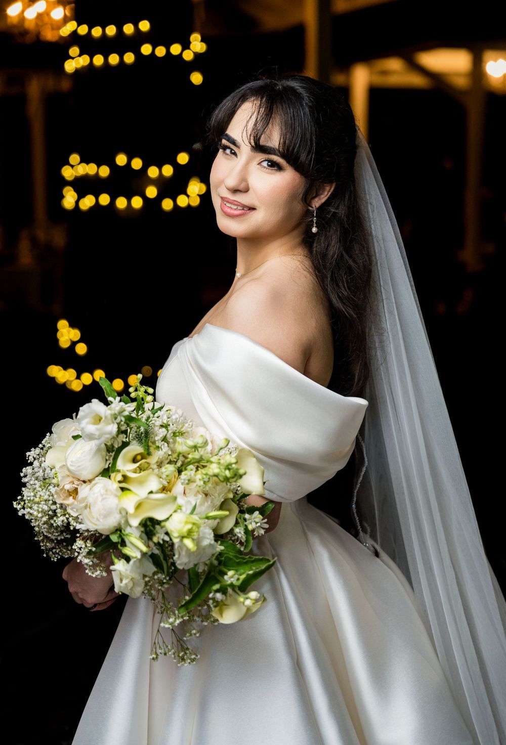 A bride in an elegant white winter wedding dress with off-shoulder neckline holds a stunning white and green bouquet.