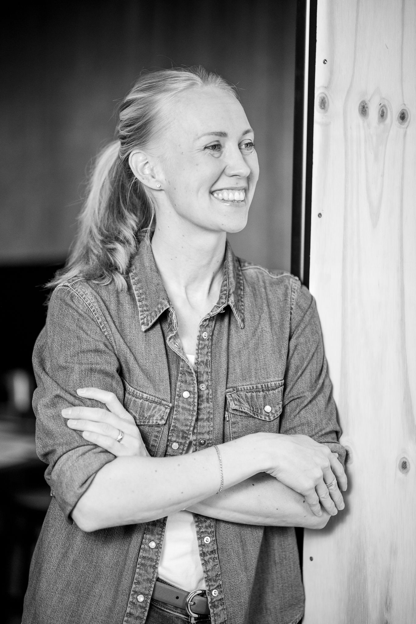 Företagsfotografering hos Studio Karlsson i Falköping. Kvinna lutar sig mot en dörrkarm och ler. Med Fotograf Veronica Eng, Mullsjö.