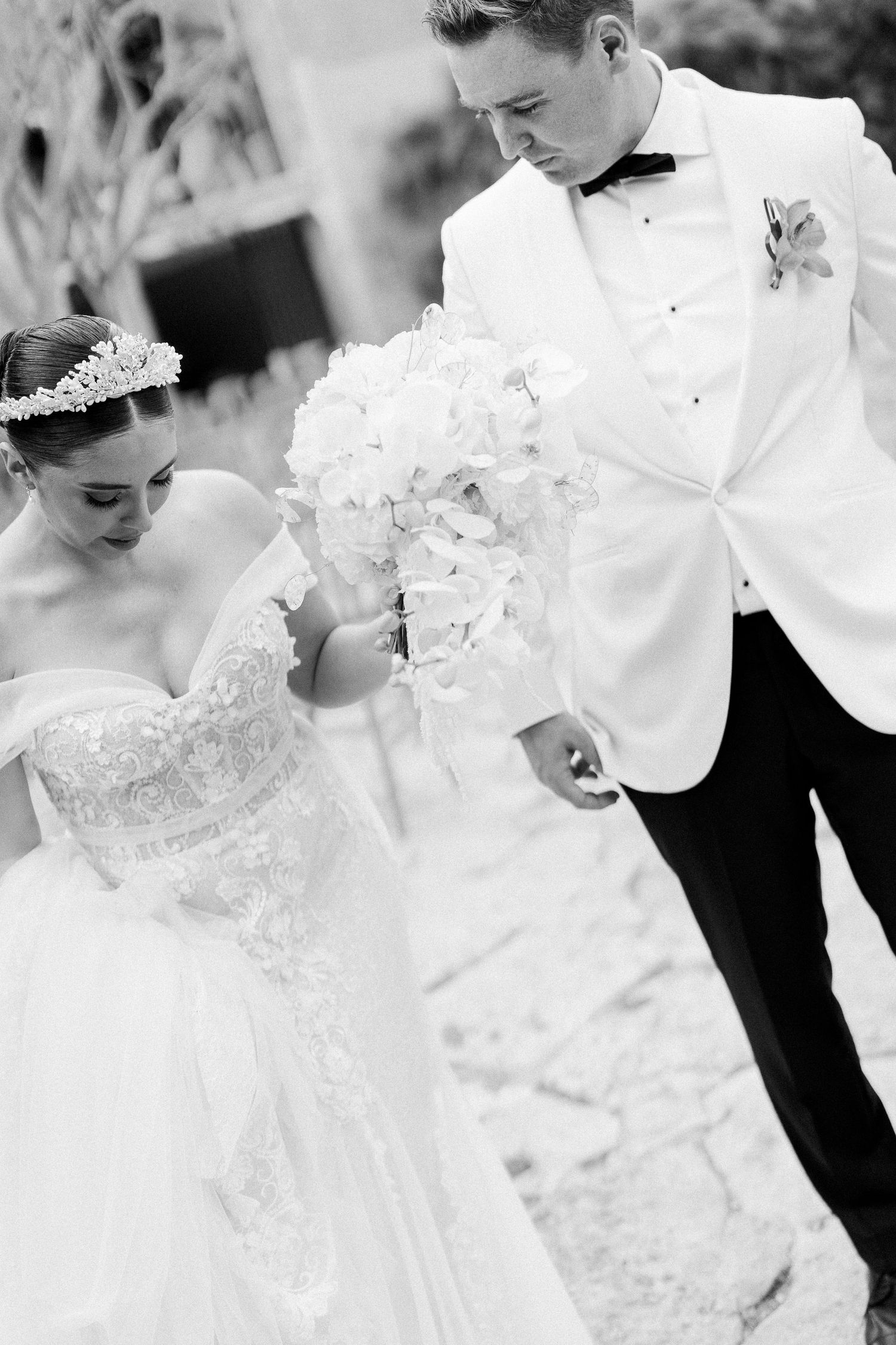 Classic black and white wedding photo showing elegant bride in lace gown with groom in white tuxedo jacket.