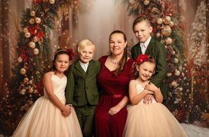 Family Christmas portrait with mother and four children in festive attire posed before holiday decorations.