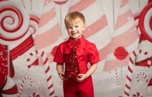 A festive holiday backdrop with candy cane stripes and swirls provides a bright setting for a joyful portrait in red attire.