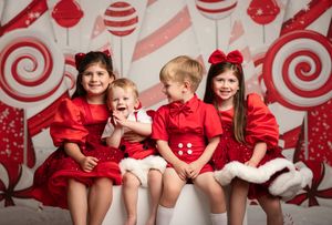 Several people in matching red shirts pose together against a white wall decorated with red candy cane-themed patterns.