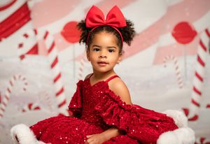 A child in a sparkly red holiday dress poses against a festive candy cane themed backdrop with hearts.