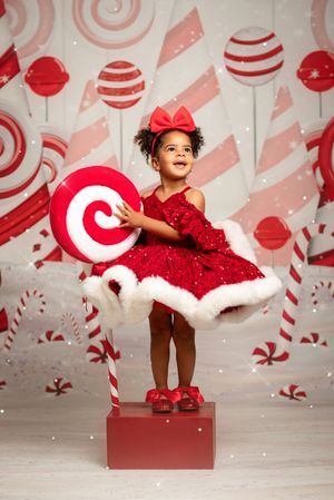 Festive holiday photo series with red and white candy cane backdrop featuring child in sparkly red dress on red platform.