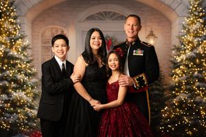 A group poses for formal holiday photos in front of decorated Christmas trees with twinkling lights and stone archways.