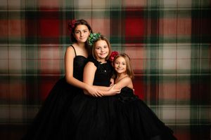 Three people in matching black formal dresses pose together against a plaid backdrop.
