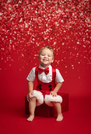 Festive holiday portrait with white shirt, red bow tie and suspenders against red background with falling glitter.