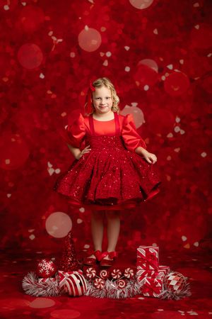 A festive holiday portrait with a red sparkly dress and Christmas decorations against a bright red bokeh background.