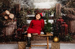 A cheerful girl in a red dress and hat sits on a bench in a festive Christmas snow scene with gifts and greenery.